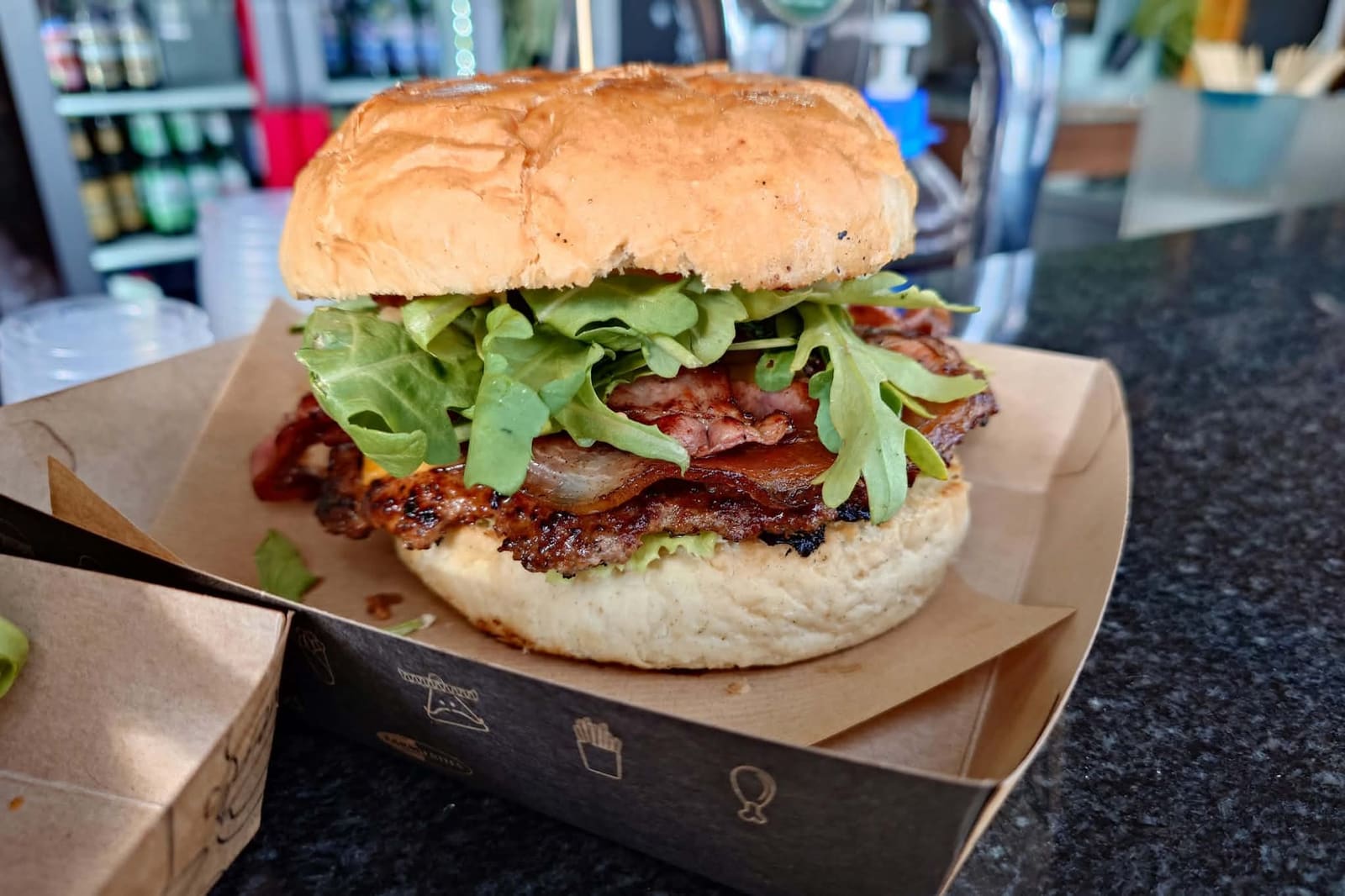 Burger z wołowiną, bekonem, cheddarem i rukolą na papierowej tacce